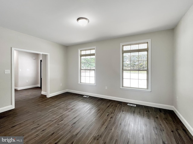 empty room featuring dark wood-style flooring, baseboards, and visible vents