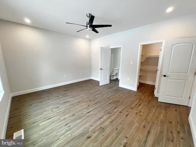 unfurnished bedroom with wood finished floors, baseboards, a spacious closet, and visible vents