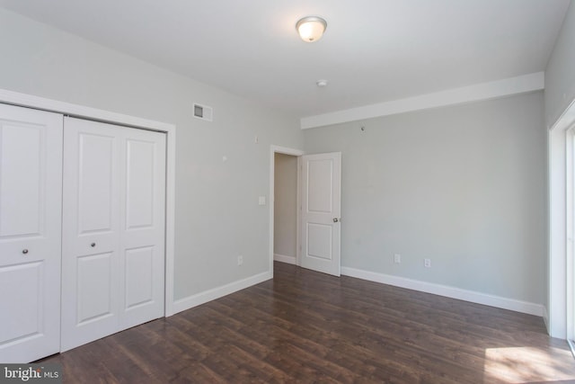 unfurnished bedroom featuring dark wood-type flooring, a closet, baseboards, and visible vents