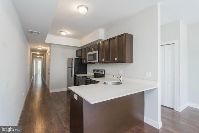 kitchen with appliances with stainless steel finishes, kitchen peninsula, sink, and dark hardwood / wood-style floors