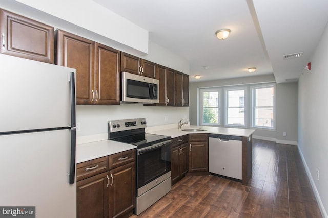 kitchen featuring dark brown cabinetry, sink, dark hardwood / wood-style flooring, kitchen peninsula, and appliances with stainless steel finishes