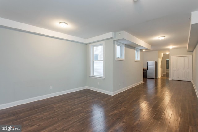 basement featuring dark wood-type flooring, baseboards, and freestanding refrigerator