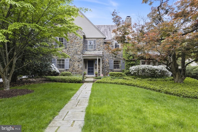 view of front of home featuring a chimney, a front lawn, and stone siding