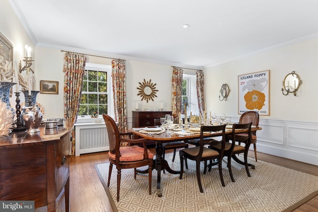 dining space with radiator heating unit, a wainscoted wall, wood finished floors, and crown molding