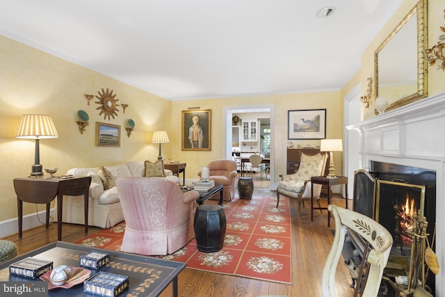 living area with a warm lit fireplace, wood finished floors, and crown molding