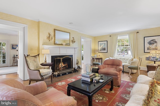 living area featuring a fireplace with flush hearth, wood finished floors, crown molding, and baseboards