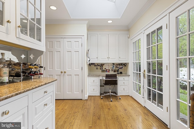 unfurnished office with built in desk, ornamental molding, a skylight, and light wood-type flooring