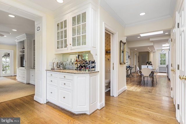 bar with wet bar, ornamental molding, light wood-style floors, and a healthy amount of sunlight