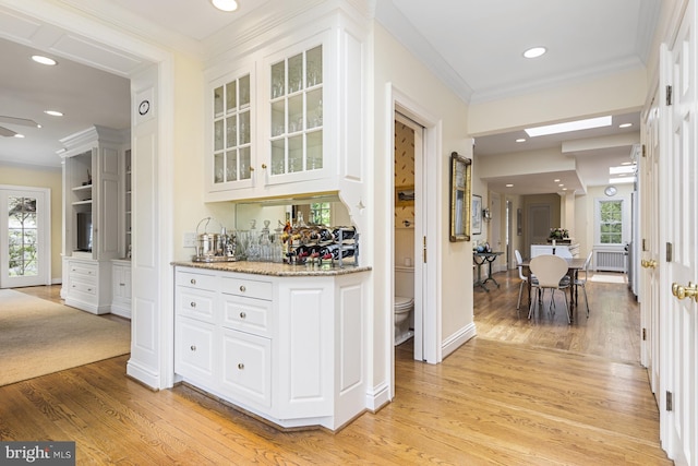 bar featuring ornamental molding, light stone countertops, white cabinetry, light hardwood / wood-style floors, and ceiling fan