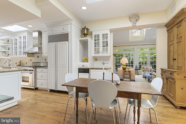 kitchen with wall chimney range hood, a sink, a skylight, high quality appliances, and decorative backsplash