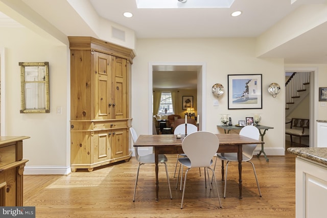dining room featuring light wood-style floors, stairway, a skylight, and baseboards