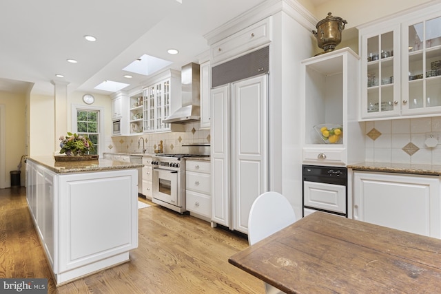 kitchen featuring white cabinets, wall chimney exhaust hood, high quality appliances, and a skylight