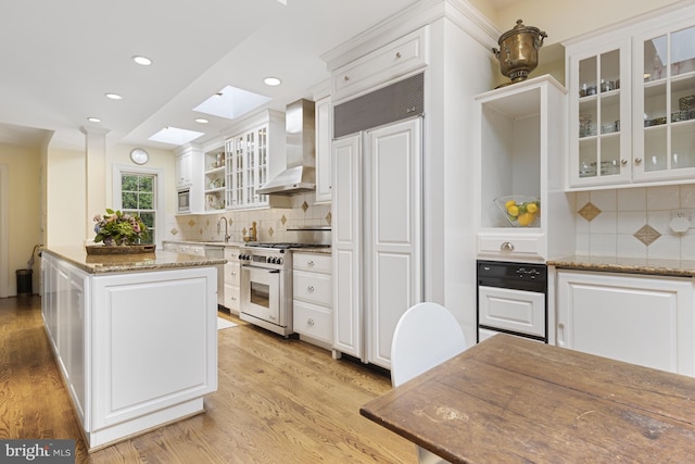 kitchen with wall chimney range hood, light hardwood / wood-style flooring, white cabinetry, and high end appliances