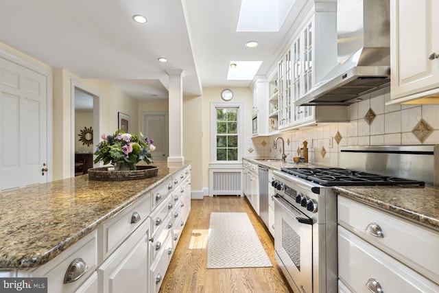 kitchen featuring wall chimney range hood, sink, light wood-type flooring, white cabinetry, and stainless steel appliances