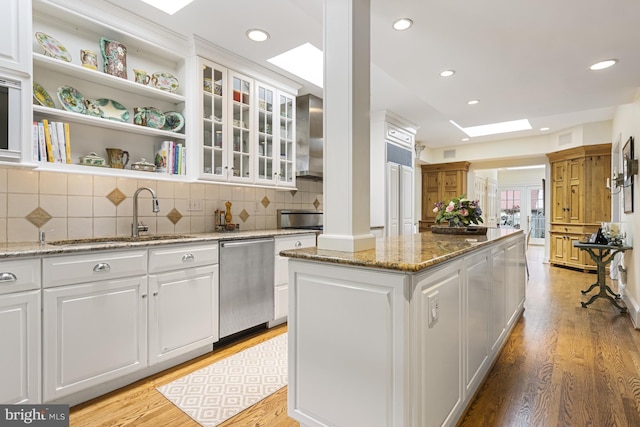 kitchen with wall chimney exhaust hood, stainless steel dishwasher, a center island, a sink, and light wood-style flooring