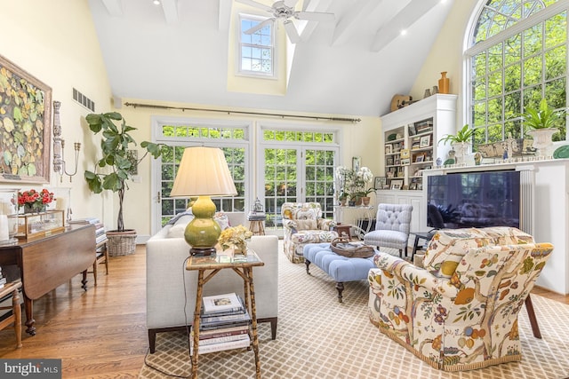 sunroom / solarium featuring a skylight, wood finished floors, visible vents, and high vaulted ceiling