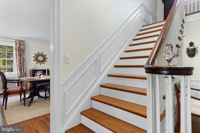 staircase featuring a wainscoted wall, wood finished floors, ornamental molding, and a decorative wall