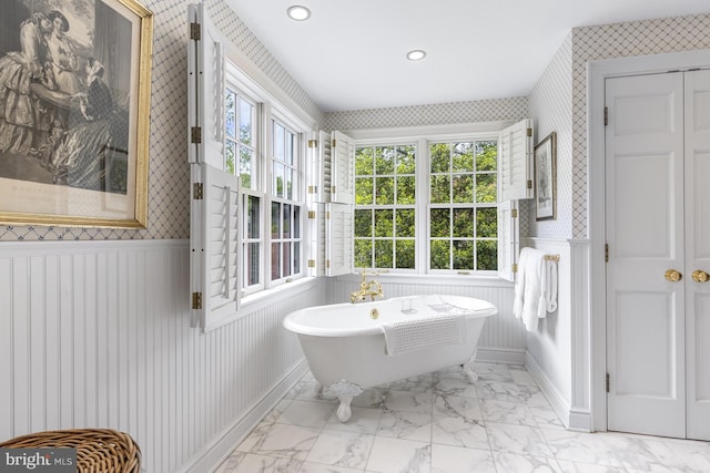 bathroom featuring a soaking tub, a wealth of natural light, a wainscoted wall, and wallpapered walls