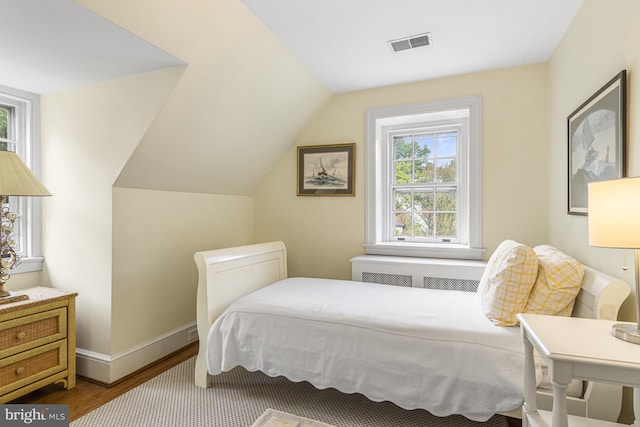 bedroom featuring lofted ceiling, radiator heating unit, and wood-type flooring