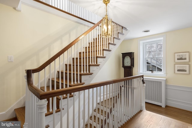 staircase with visible vents, a wainscoted wall, wood finished floors, and a notable chandelier