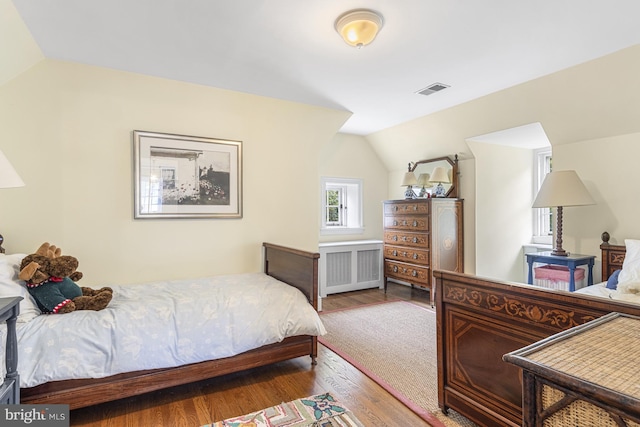 bedroom featuring radiator heating unit, visible vents, lofted ceiling, and wood finished floors