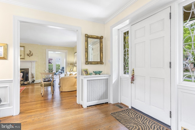 foyer featuring a warm lit fireplace, light wood-style flooring, visible vents, and crown molding