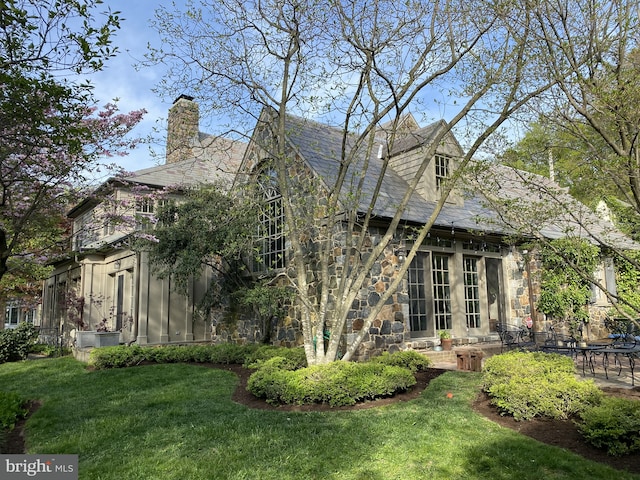 rear view of property with stone siding, a sunroom, a yard, and a patio