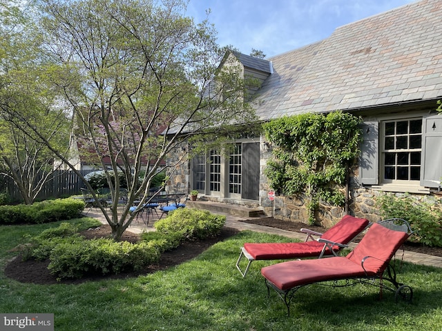 back of house featuring fence, a yard, a high end roof, a patio area, and stone siding