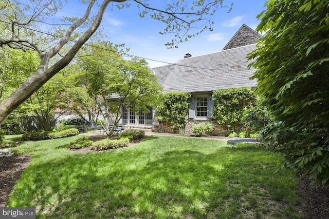 exterior space with a lawn, a high end roof, stone siding, and french doors