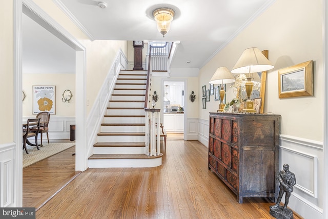stairs featuring wainscoting, a decorative wall, ornamental molding, and wood finished floors
