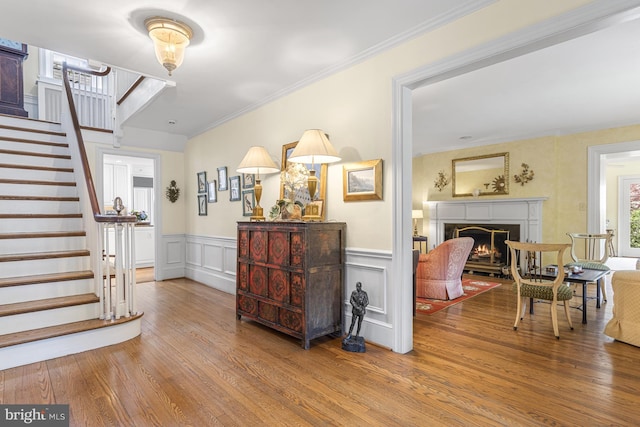 foyer with wainscoting, a lit fireplace, wood finished floors, stairs, and ornamental molding