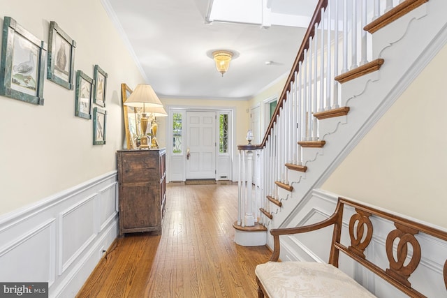 foyer featuring a wainscoted wall, wood finished floors, stairs, a decorative wall, and ornamental molding