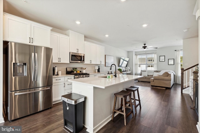 kitchen with dark hardwood / wood-style floors, sink, white cabinetry, appliances with stainless steel finishes, and a center island with sink