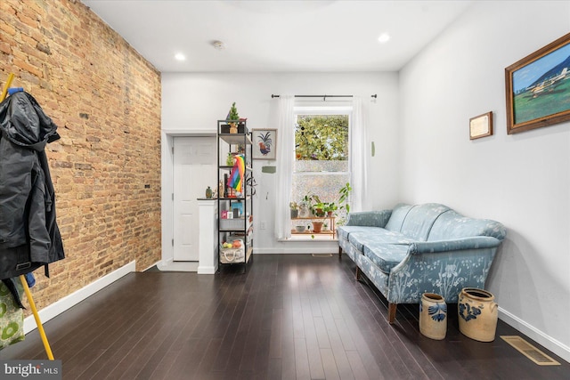 living area featuring dark wood-type flooring and brick wall