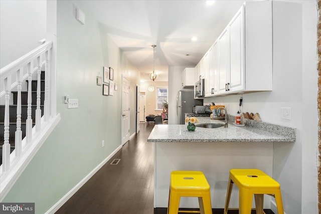 kitchen with appliances with stainless steel finishes, light stone counters, a breakfast bar area, dark hardwood / wood-style floors, and white cabinets