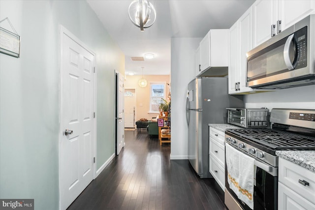 kitchen featuring white cabinetry, appliances with stainless steel finishes, decorative light fixtures, and light stone counters