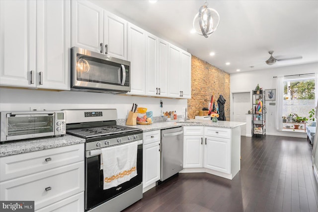 kitchen with white cabinets, appliances with stainless steel finishes, dark hardwood / wood-style floors, and decorative light fixtures