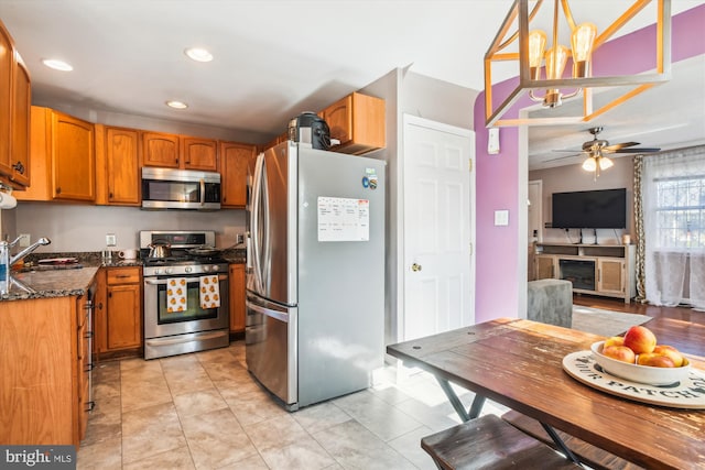 kitchen with stainless steel appliances, dark stone counters, sink, decorative light fixtures, and ceiling fan with notable chandelier