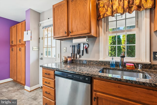 kitchen with sink, light tile patterned floors, dark stone counters, and stainless steel dishwasher