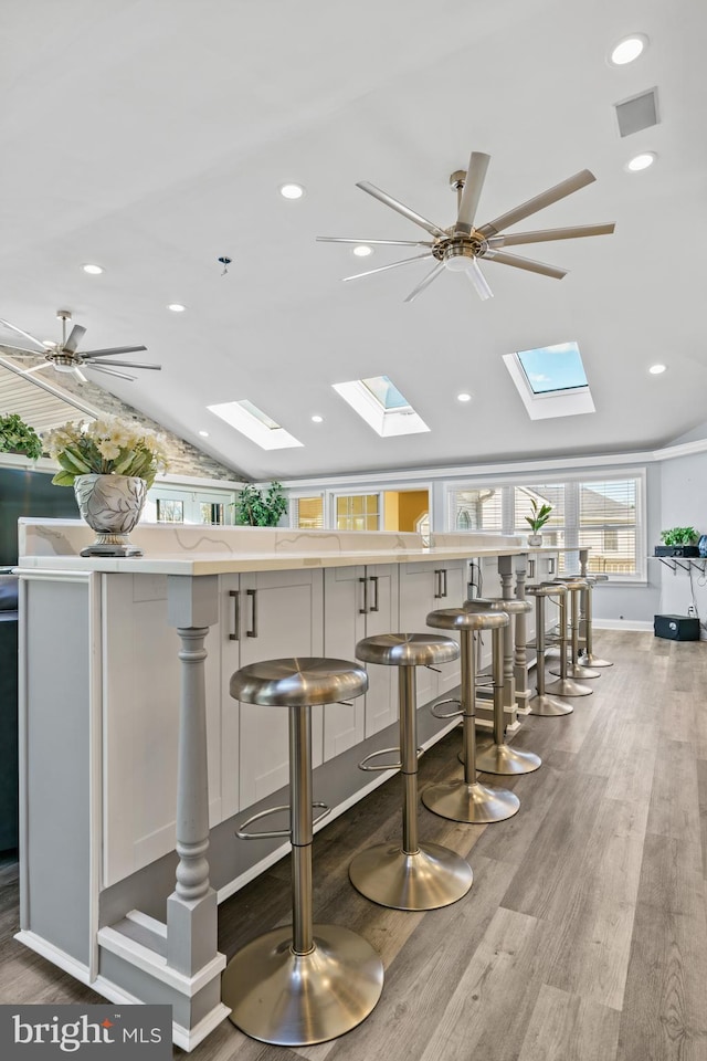 bar with white cabinets, hardwood / wood-style flooring, and vaulted ceiling with skylight