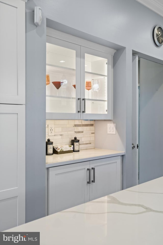 bar with light stone counters, decorative backsplash, and white cabinetry