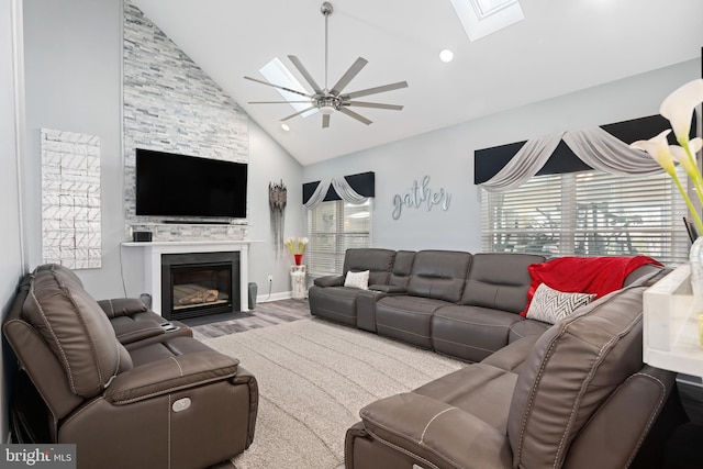 living room featuring ceiling fan, a skylight, wood-type flooring, a stone fireplace, and high vaulted ceiling