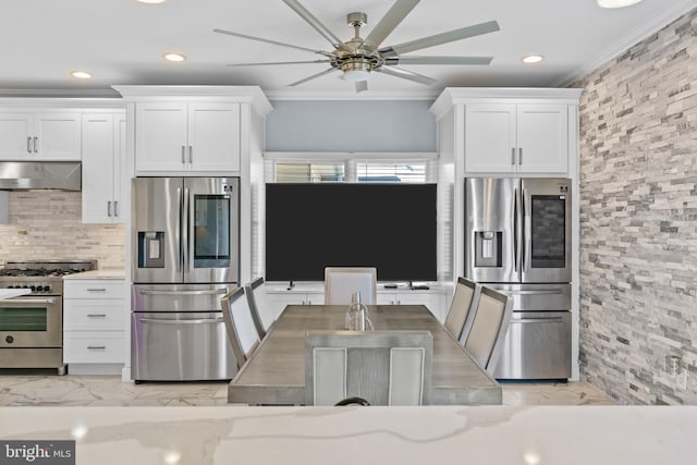 kitchen featuring light stone counters, wall chimney range hood, white cabinetry, and stainless steel appliances