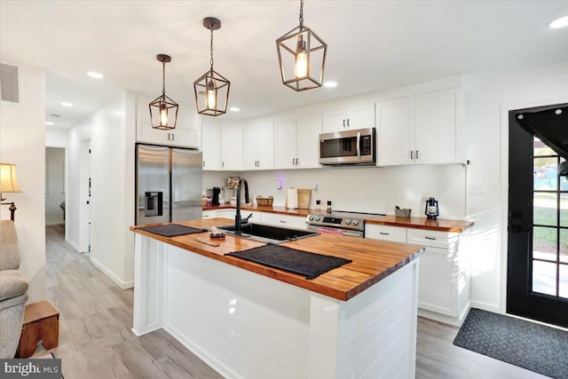 kitchen with sink, appliances with stainless steel finishes, white cabinets, and butcher block counters