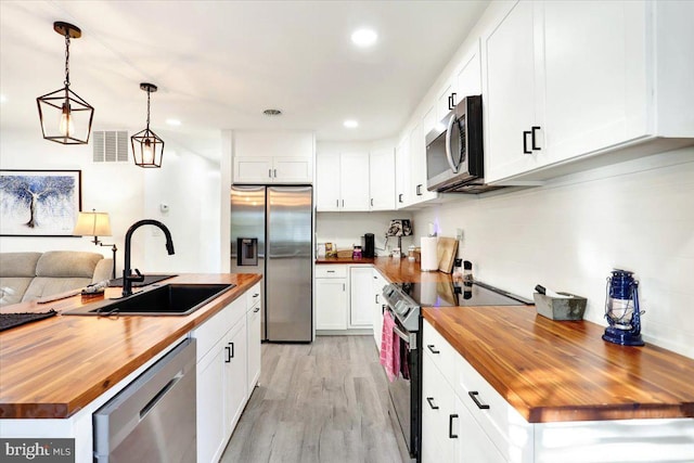 kitchen with white cabinetry, stainless steel appliances, decorative light fixtures, and butcher block countertops