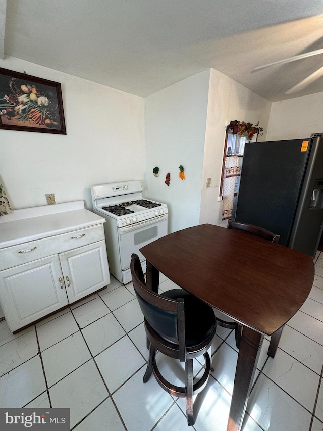 kitchen with stainless steel fridge, white cabinetry, light tile patterned floors, and gas range gas stove