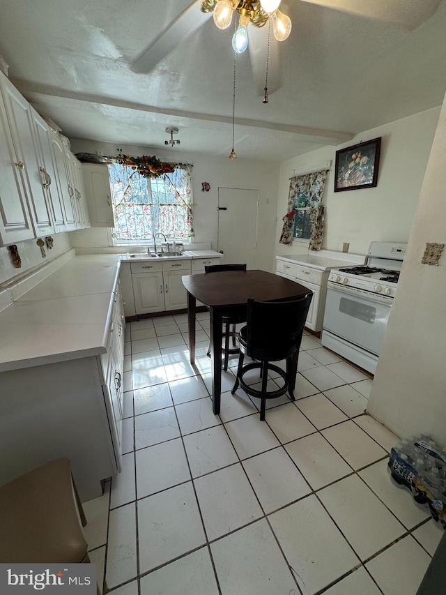 kitchen with sink, white range with gas stovetop, ceiling fan, white cabinets, and light tile patterned floors