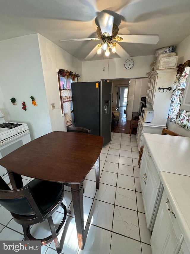 kitchen with stainless steel refrigerator with ice dispenser, white gas stove, light tile patterned flooring, white cabinets, and ceiling fan