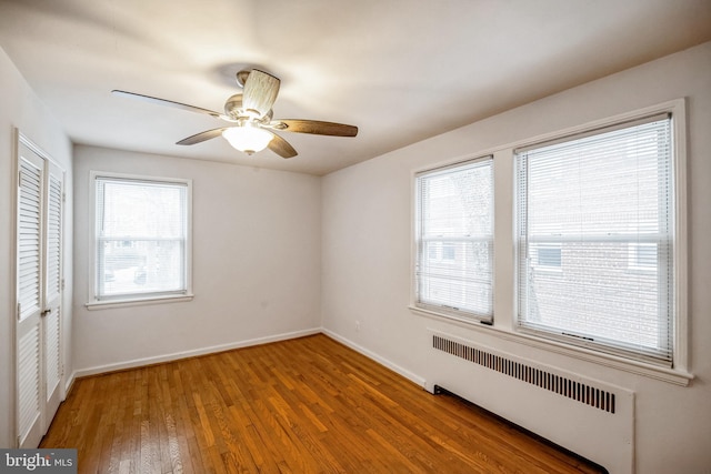 unfurnished bedroom featuring wood-type flooring, radiator, a closet, ceiling fan, and multiple windows