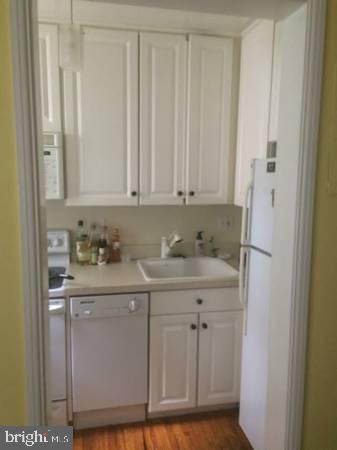 kitchen with white cabinetry, sink, white appliances, and hardwood / wood-style flooring